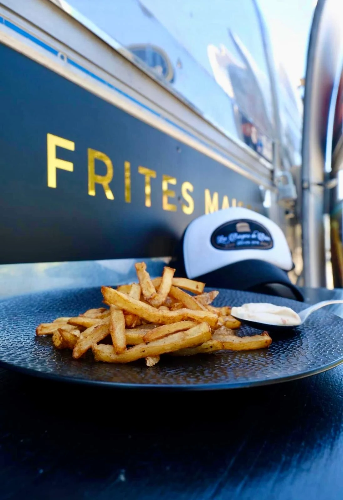 Frites maison et sauce maison devant l'Airstream, avec la casquette Les Burgers de Brice